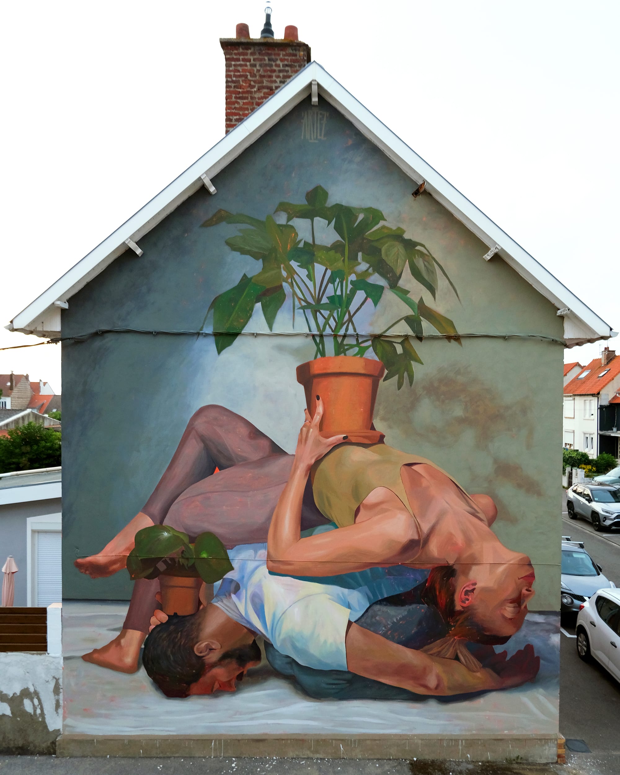 a mural on the side of a residential building of two figures laying on the ground, one holding a house plant