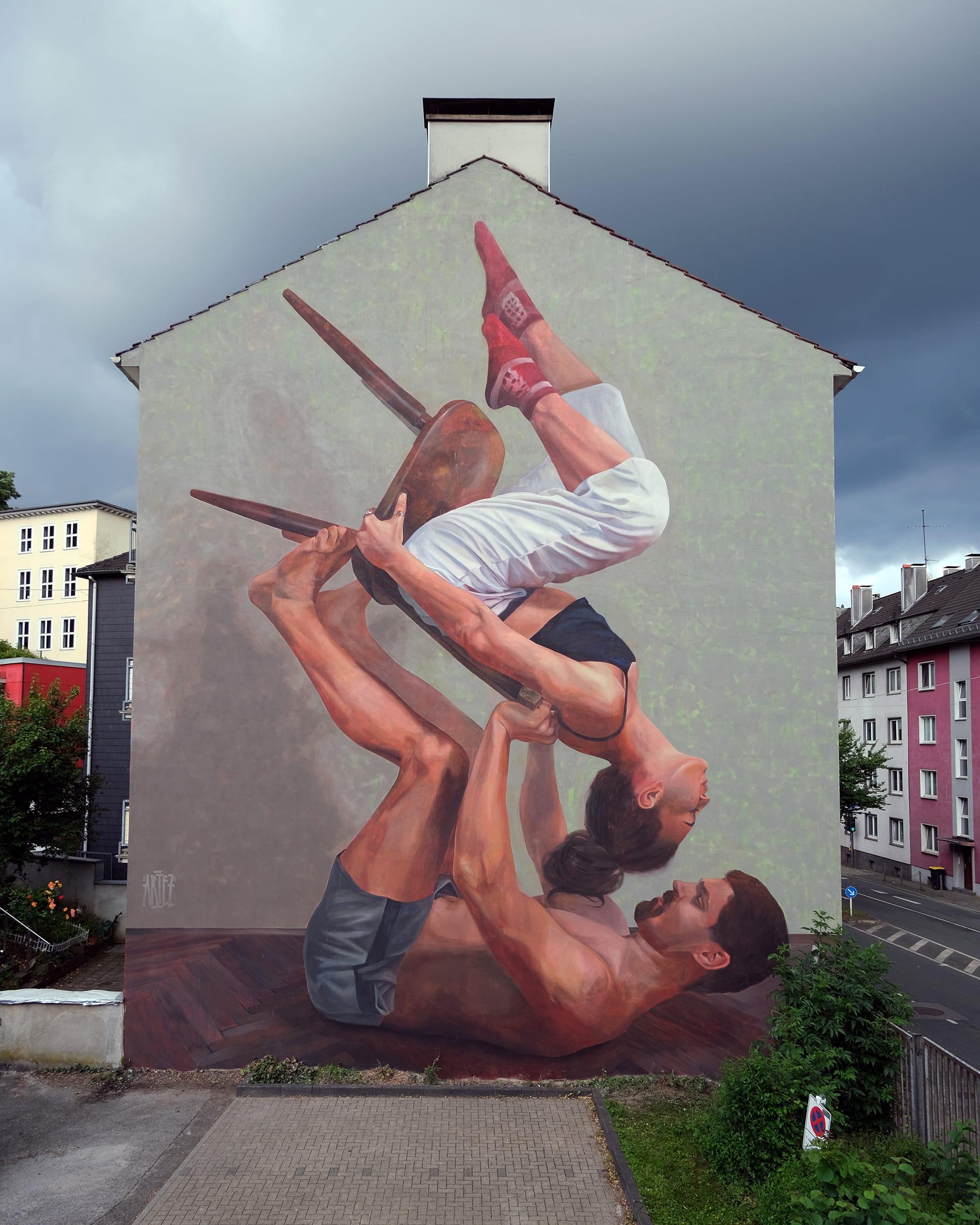 a mural on the side of a residential building of two dancers balancing with a chair