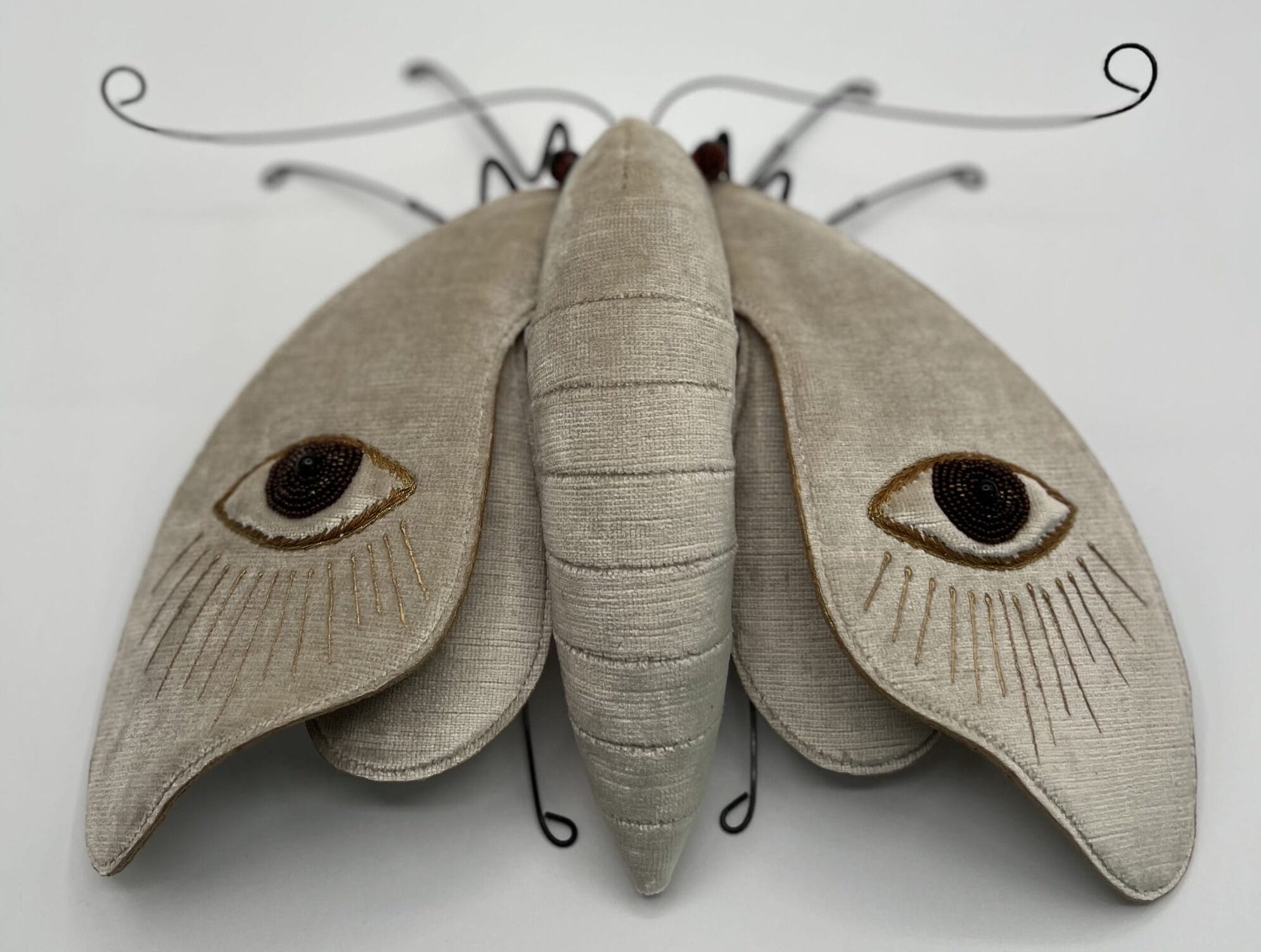 a moth sculpture made from textile and wire, with eyes on the wings