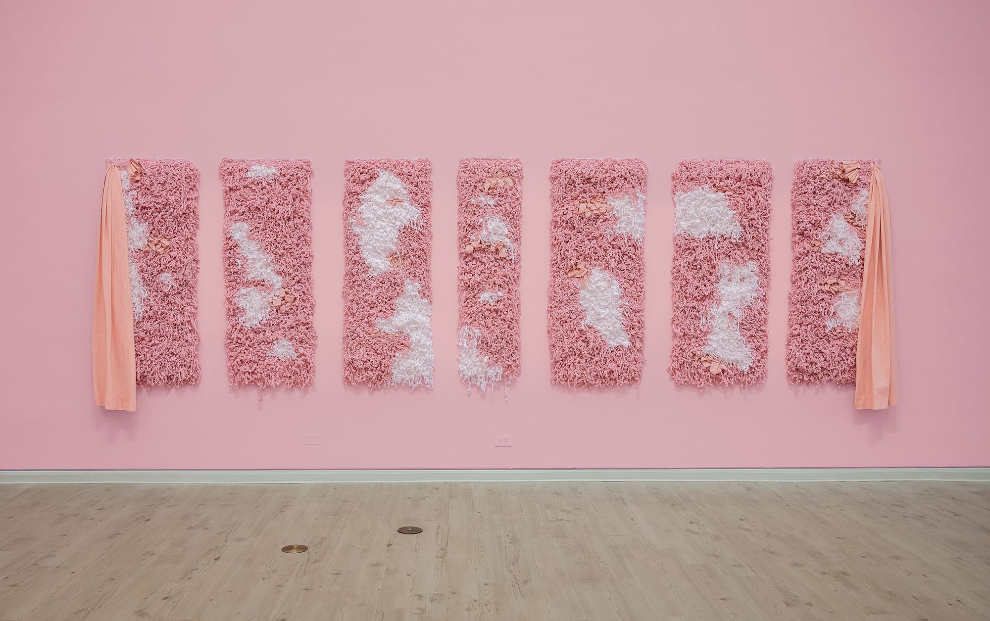 an installation view of 7 fluffy pink and white tapestries by Bryana Bibbs