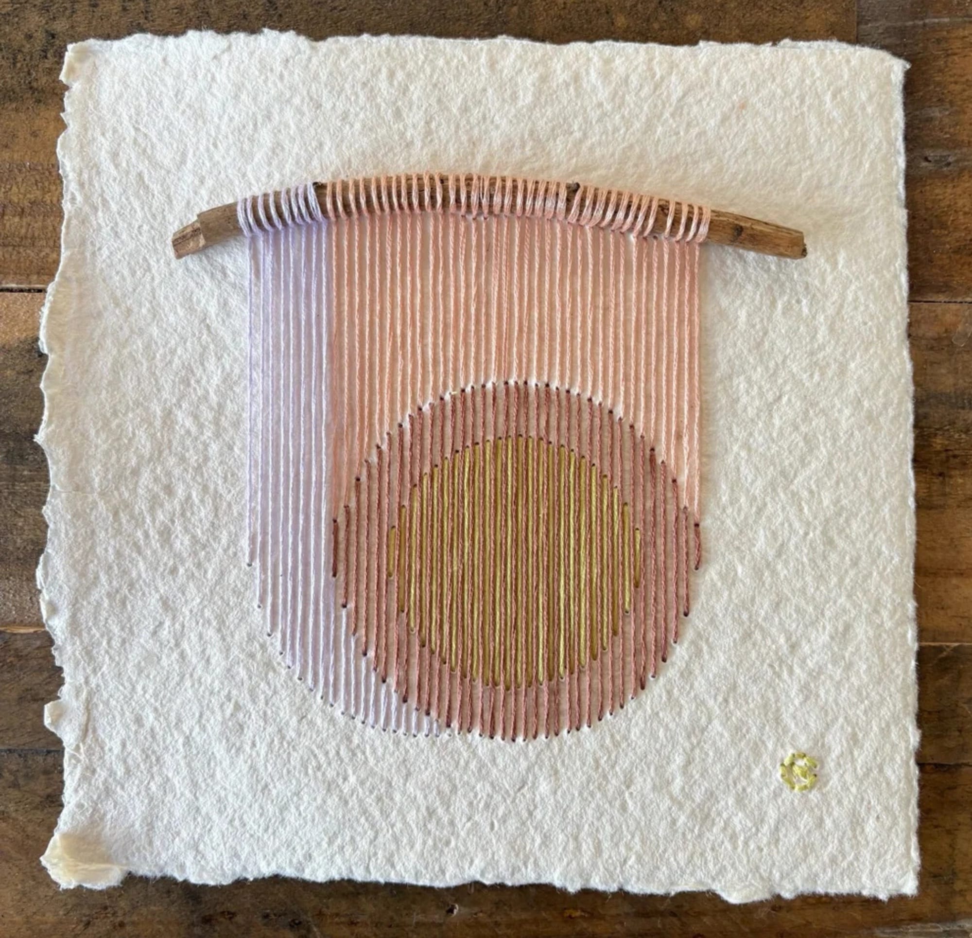 a paper artwork by Natalie Ciccoricco featuring handmade paper and pink and ochre thread wound around found twigs in a geometric shape