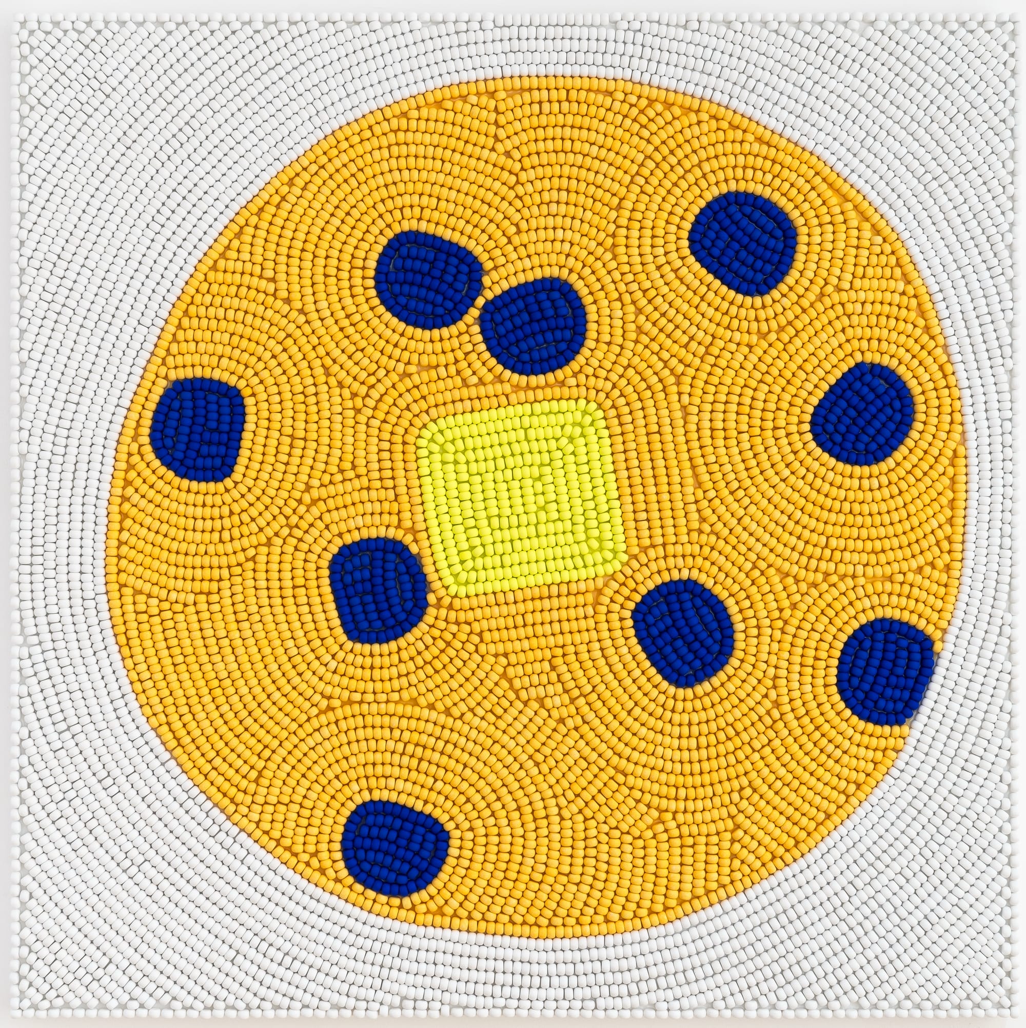 a wooden bead piece by Renee Condo of a yellow circle with blue dots and a lighter yellow square at the center
