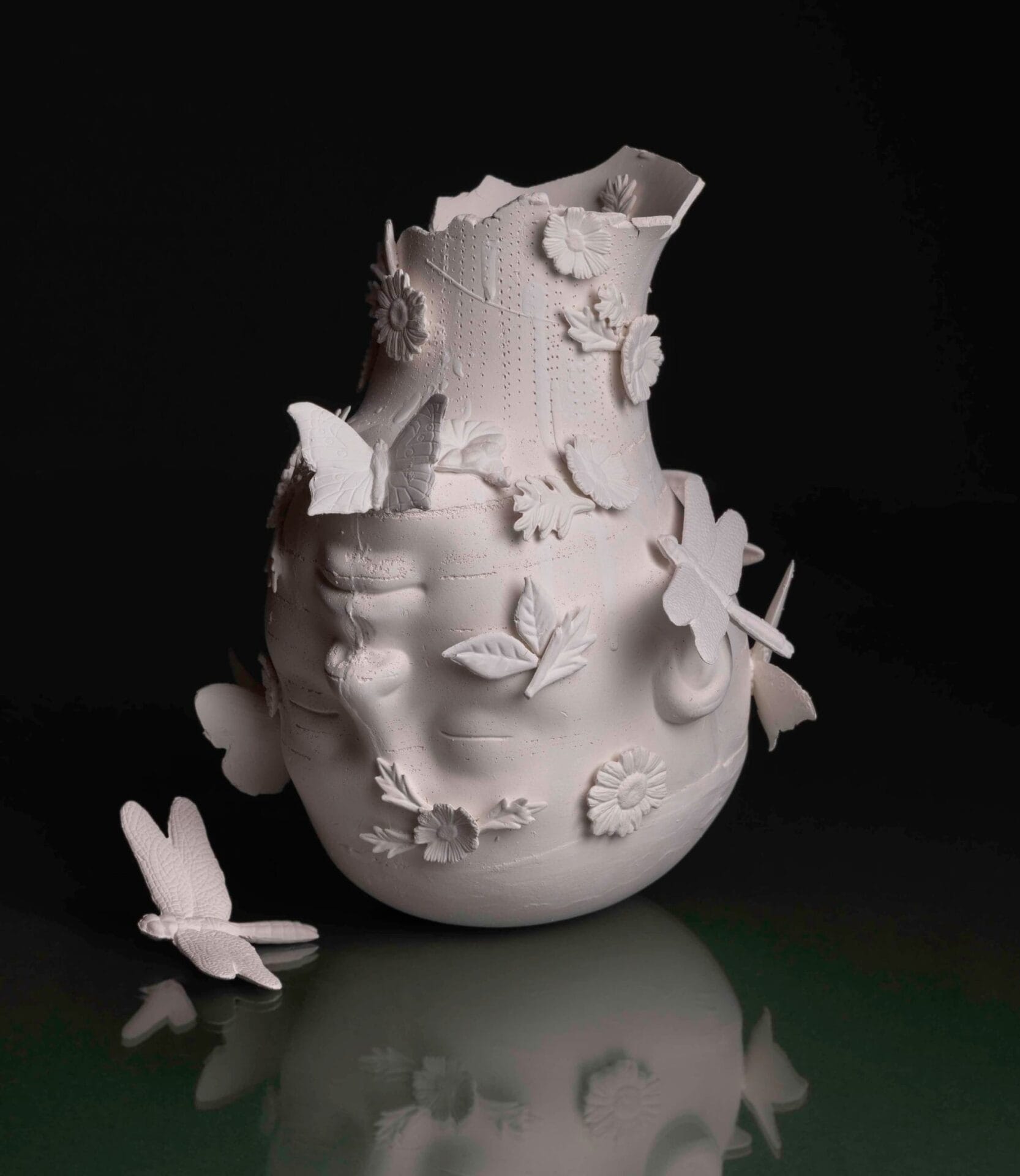 an upside down head of white porcelain rests on a table with insects and flowers around it