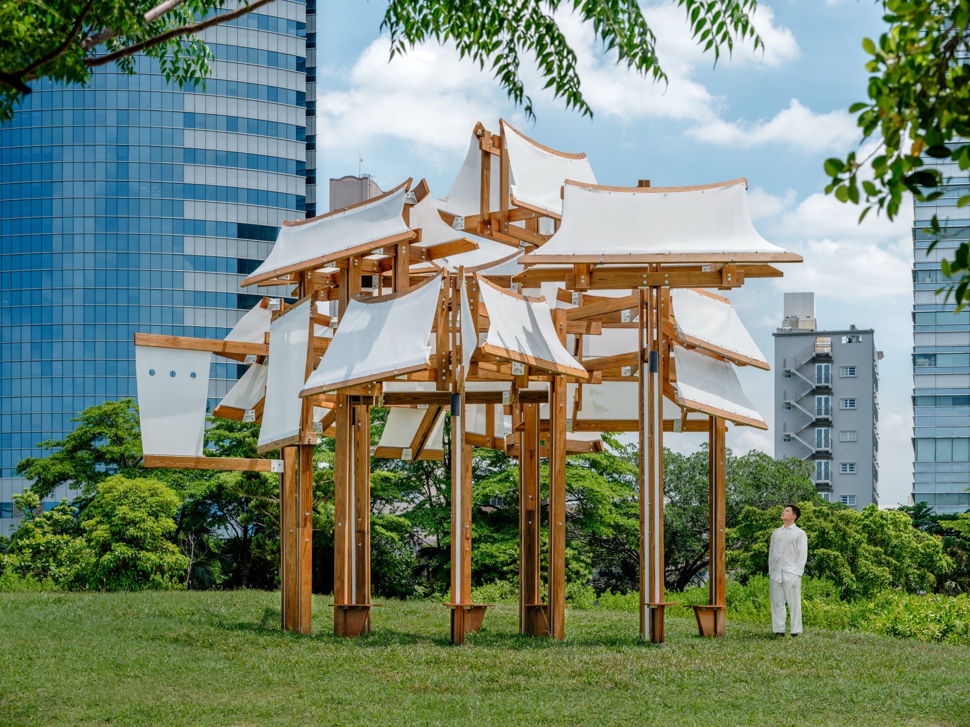 a pavilion by designer Cheng-Tsung Feng made of wood, iron, and canvas, which loosely resembles ship sails with a man standing by for scale