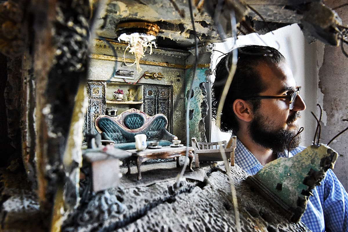 an image of mohamed hafez next to a miniature home marred by war