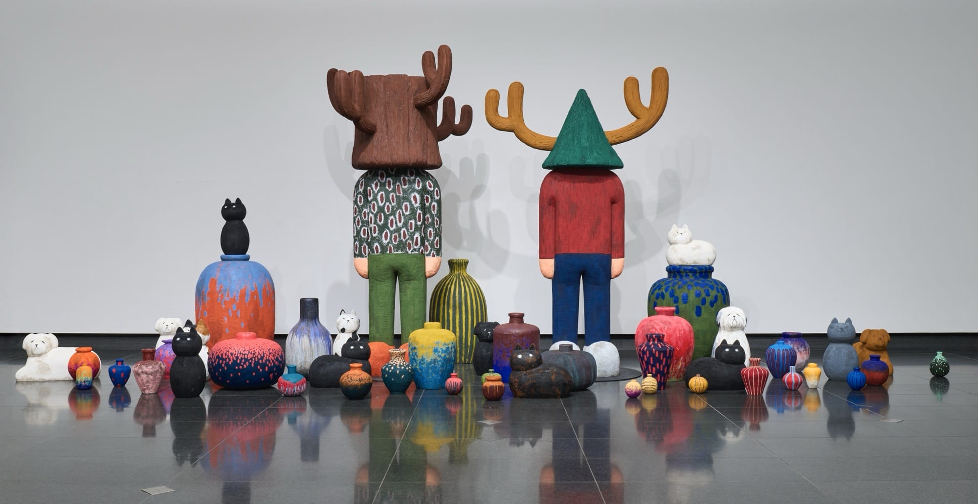 a sculptural installation by Yuichi Hirako of two oversized cartoonish figures with antler-like head coverings, with numerous vases at their feet