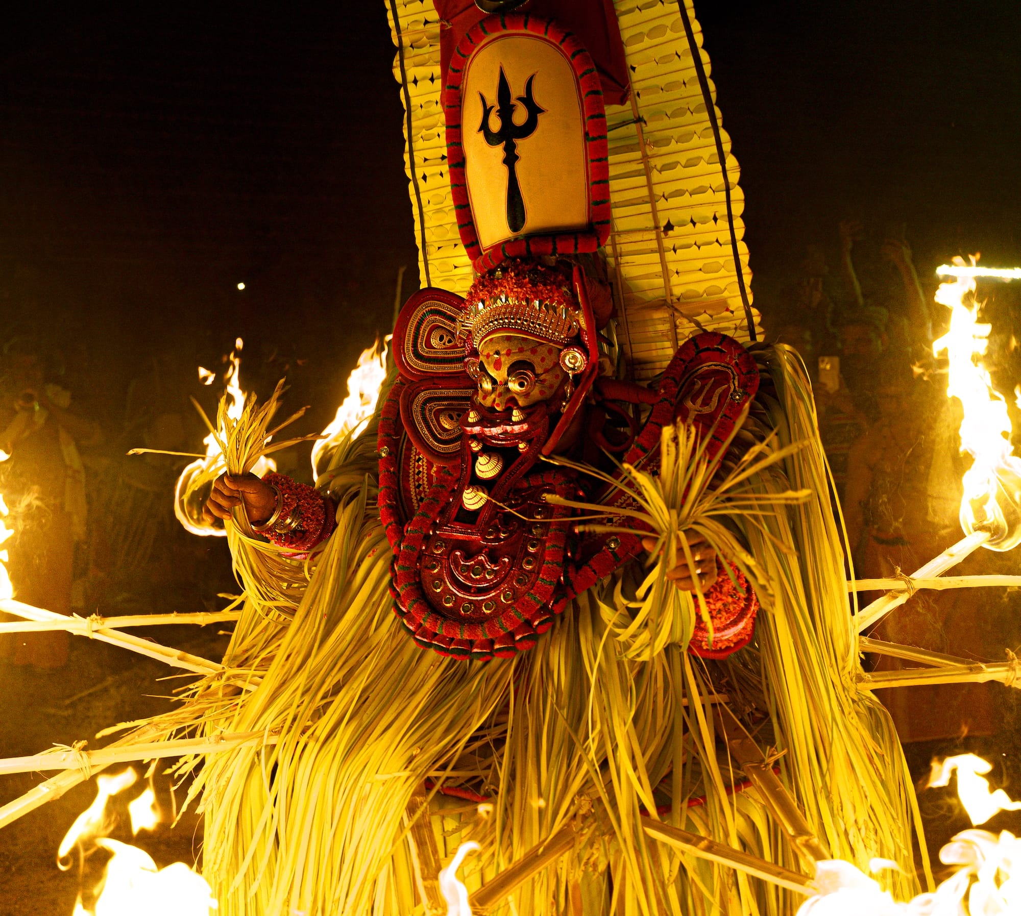 a photograph by Navneet Jayakumar of an elaborate ceremonial event around a fire, focused on an outfit worn by a performer for Theyyam, in Kerala, India