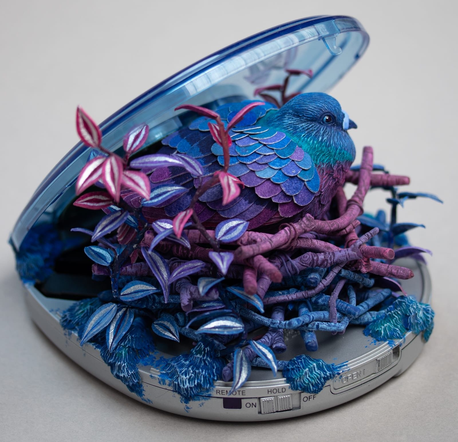 a sculpture by Stéphanie Kilgast of a colorful bird nesting inside of a portable CD player