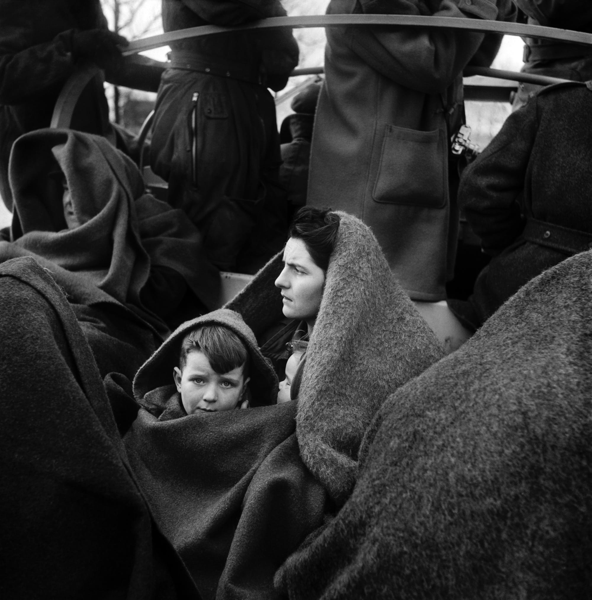 a black and white photo of a little boy and his mother huddled under blankets
