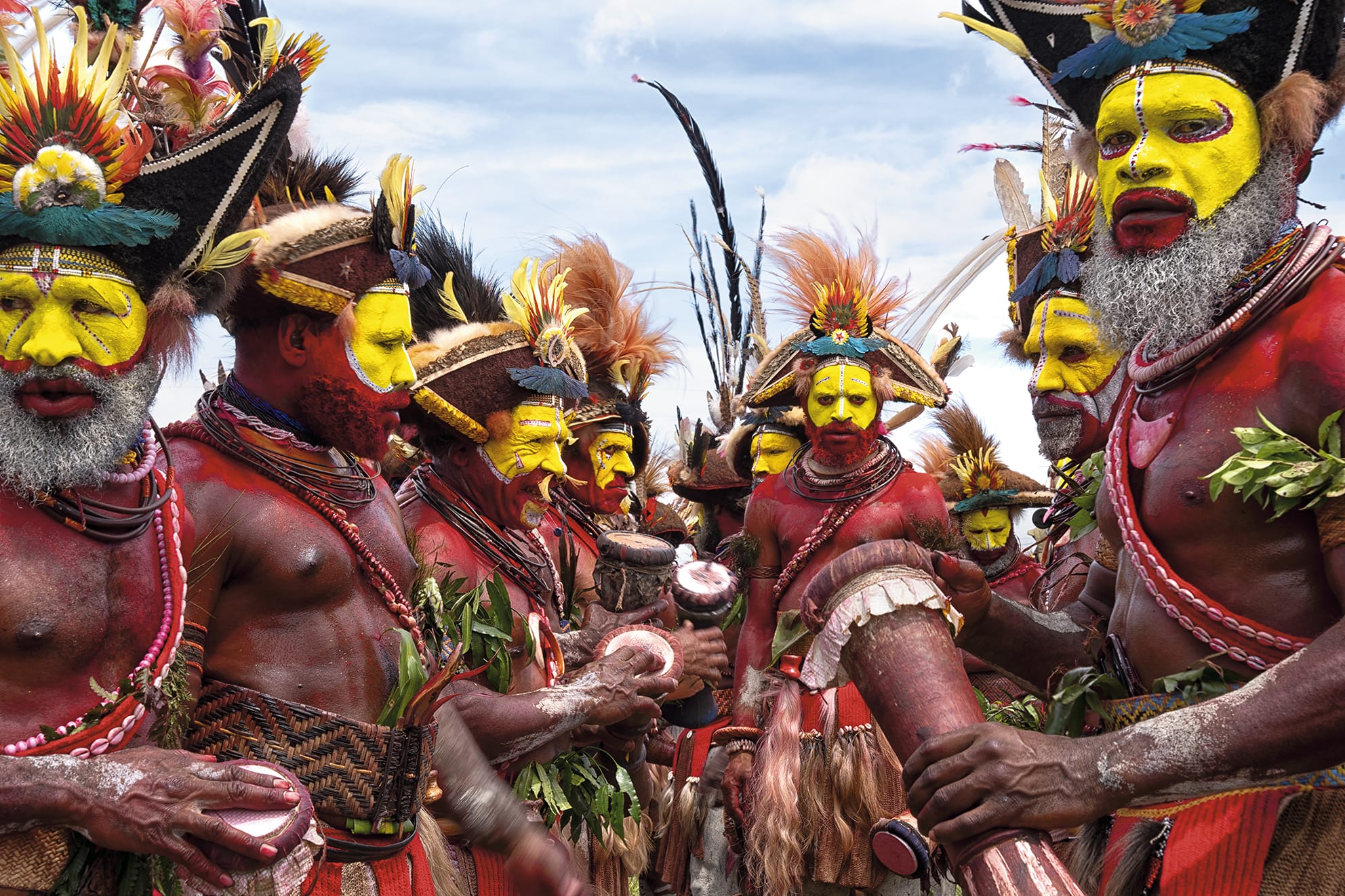 a group of Indigenous Papua New Guinean men with yellow facepaint and elaborate headdresses and regalia