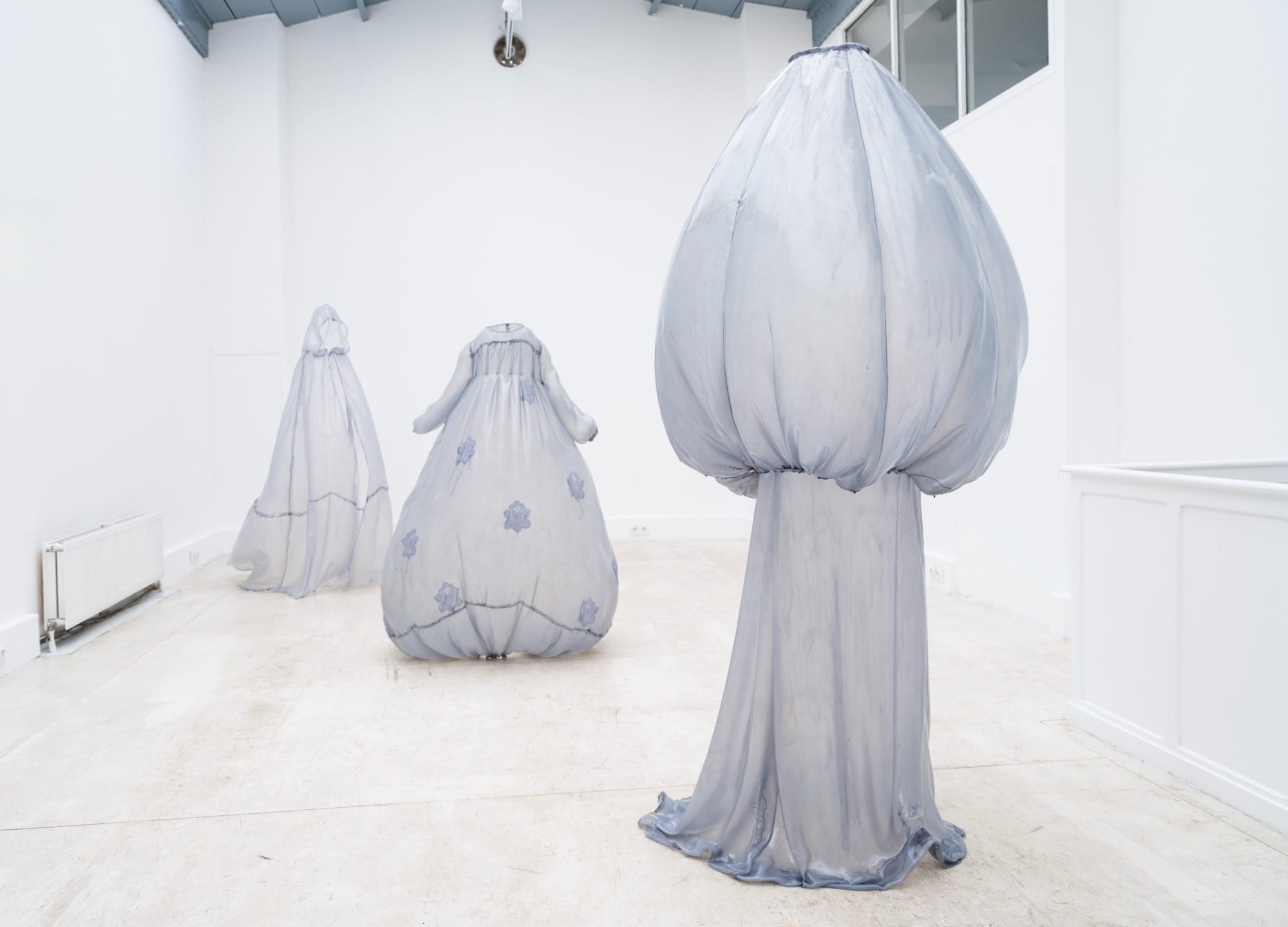 a collection of stiff pale blue fiberglass victorian style dresses by Brandon Morris that stand without wearers in the middle of a gallery