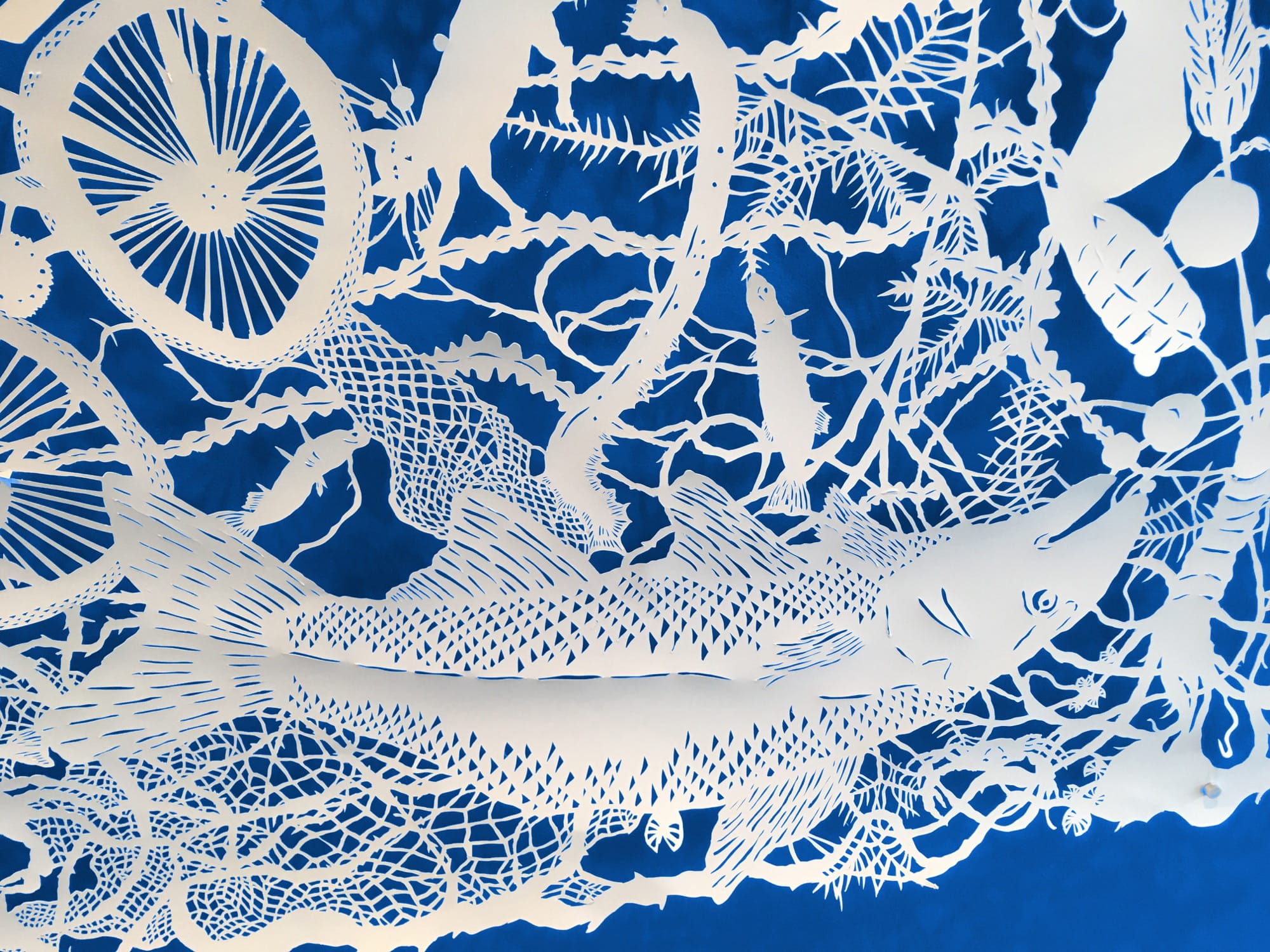 a detail of a composition of botanic motifs, human figures, and a fish made of cut paper on a dark blue background that has been painted onto a wall