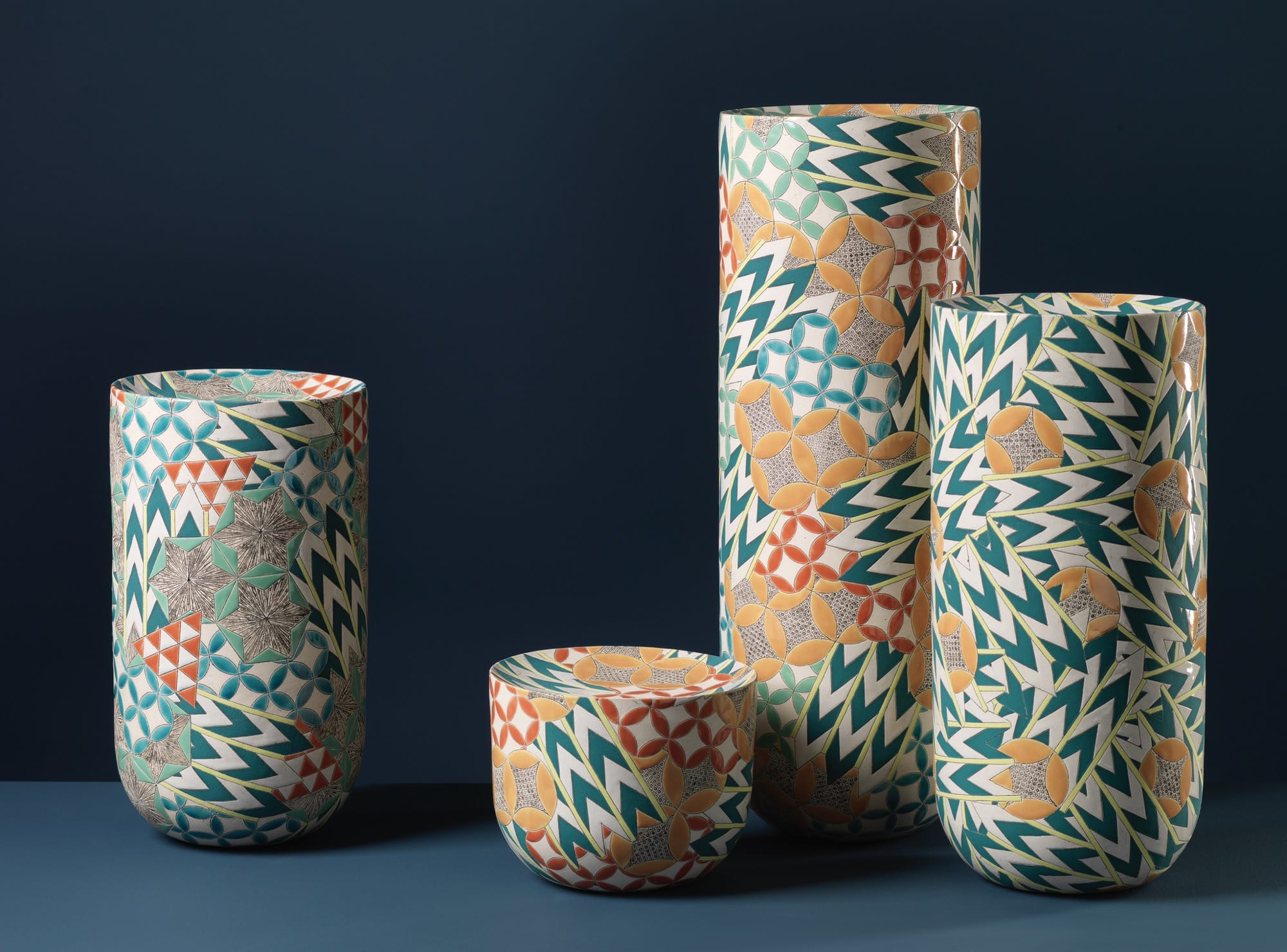 four colorful, geometrically patterned, cylindrical ceramic forms