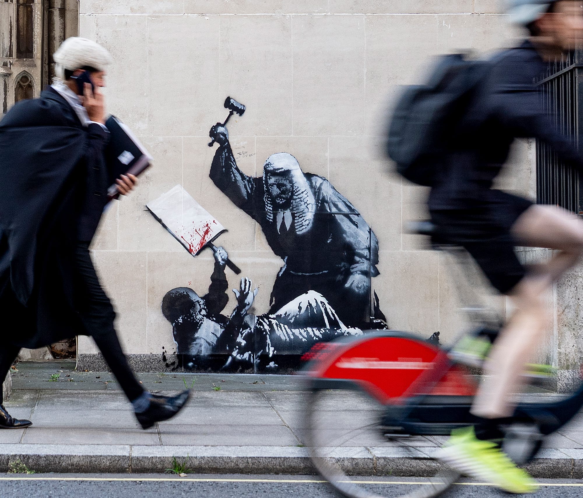 a barrister walks by the Royal Courts of London, where a spraypainted image by Banksy on the wall depicts a judget violently attacking a pro-Palestine protestor