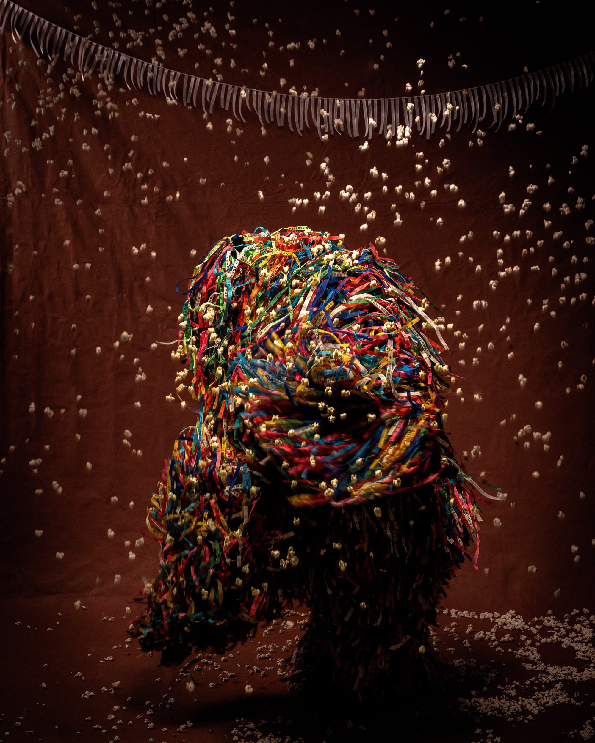 a photograph of a dancing, costumed figure with long strands of colorful fabric whipping in the air