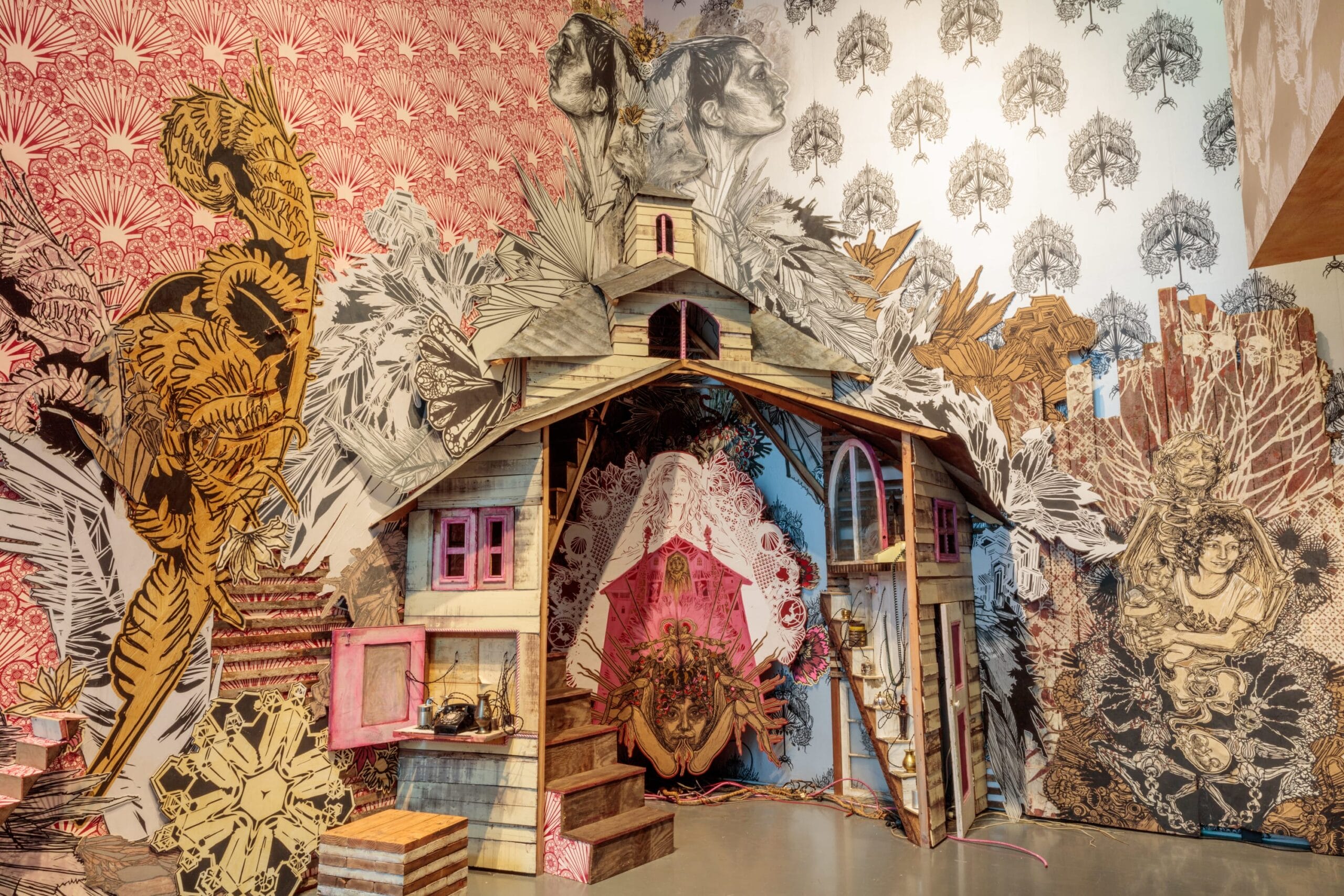 an installation with patterned wallpaper, figures, vignettes, and a tarantula woman at the center