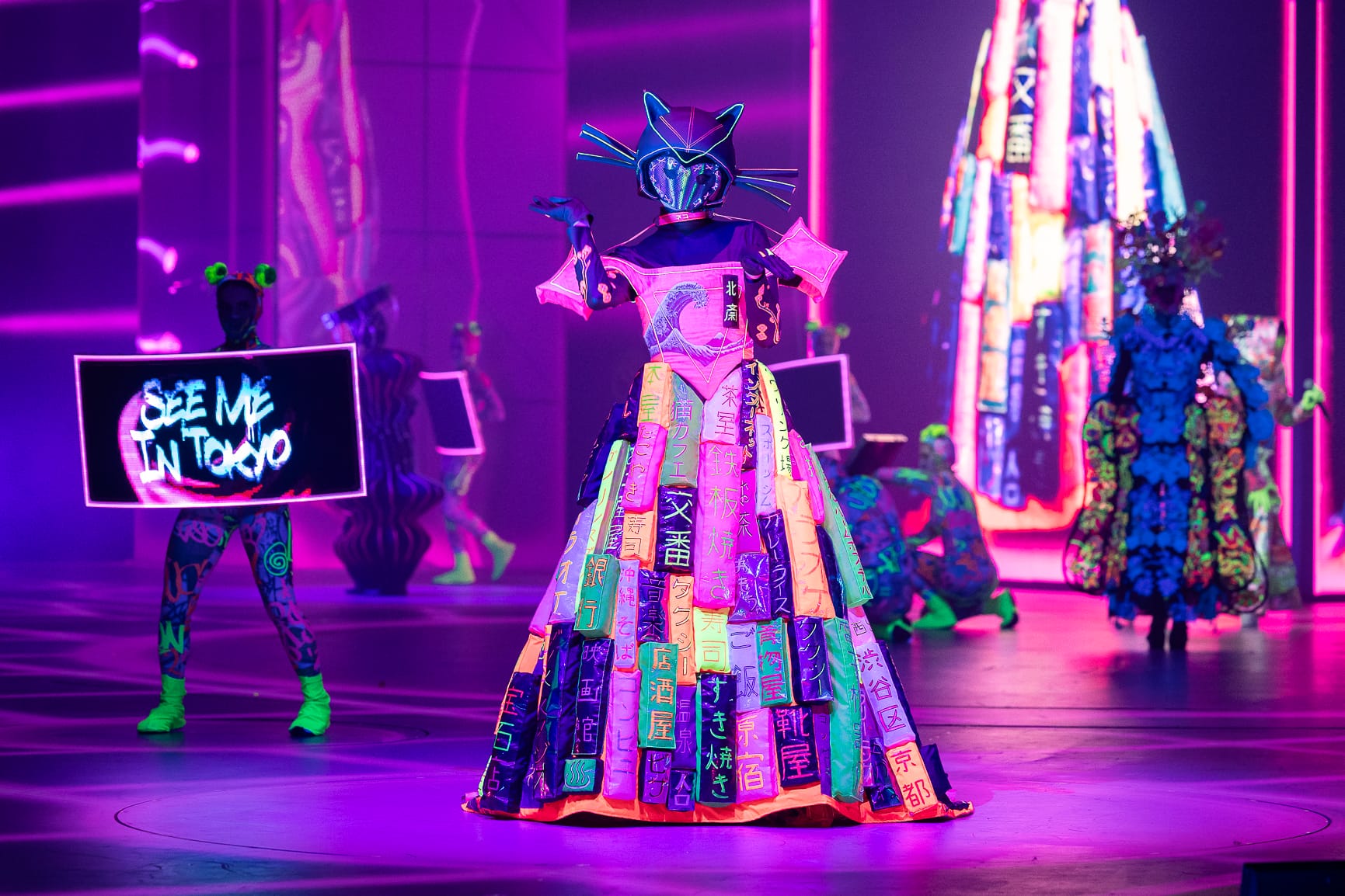 an elaborate costume with Japanese writing on the fabric, glowing under black light, worn by a performer on stage